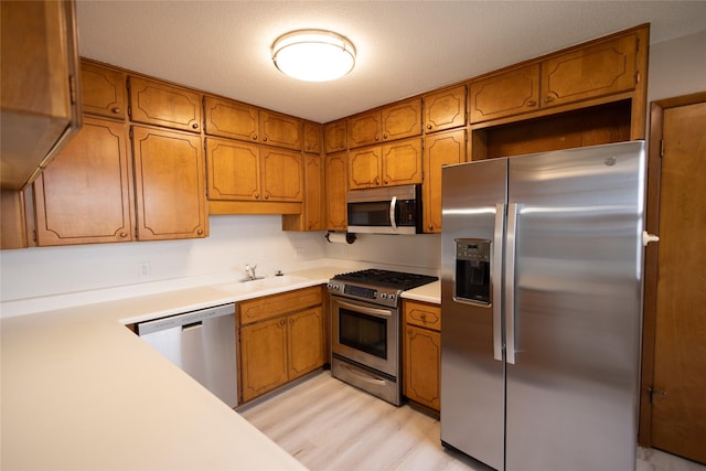 kitchen with light countertops, a sink, appliances with stainless steel finishes, and brown cabinets