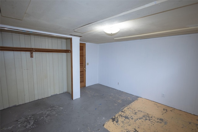 unfurnished bedroom with a closet, wooden walls, and unfinished concrete flooring