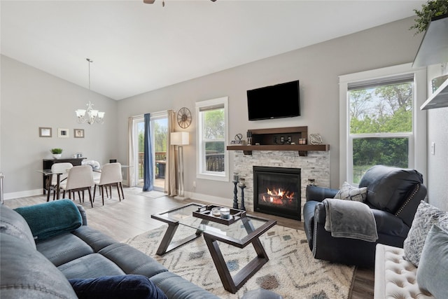 living room featuring lofted ceiling, a fireplace, baseboards, light wood-style flooring, and ceiling fan with notable chandelier