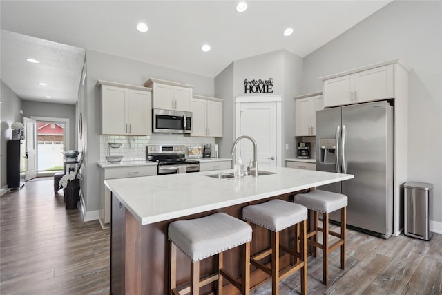 kitchen with appliances with stainless steel finishes, a sink, a kitchen breakfast bar, wood finished floors, and backsplash