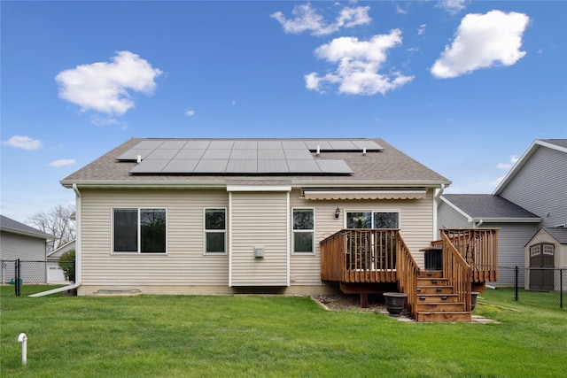 rear view of house with a fenced backyard, roof mounted solar panels, a wooden deck, and a yard