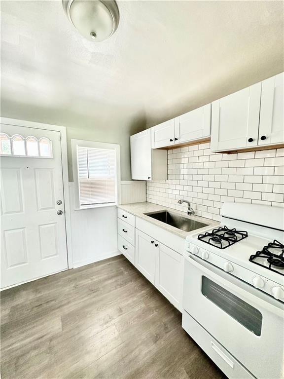 kitchen featuring wood finished floors, white gas stove, light countertops, white cabinetry, and a sink