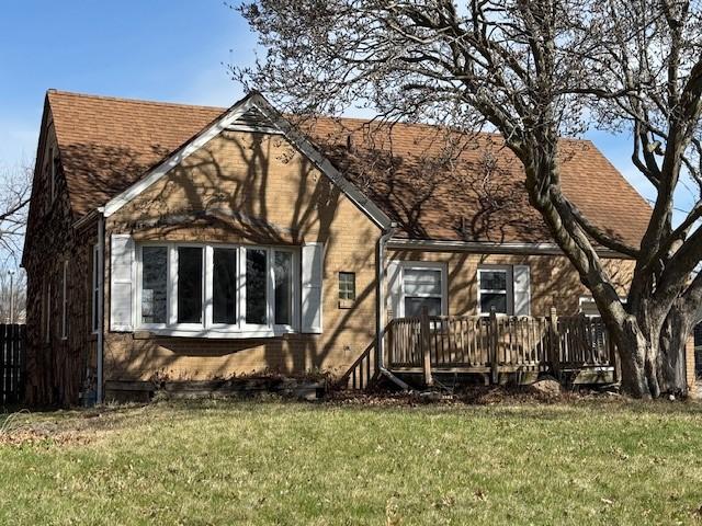 tudor home with brick siding, a deck, a shingled roof, and a front lawn