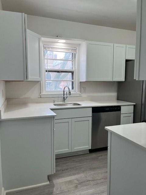 kitchen with stainless steel dishwasher, light wood-type flooring, a sink, light countertops, and freestanding refrigerator
