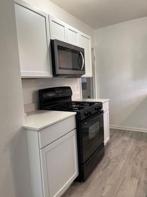 kitchen featuring black gas range, light countertops, stainless steel microwave, and light wood-type flooring