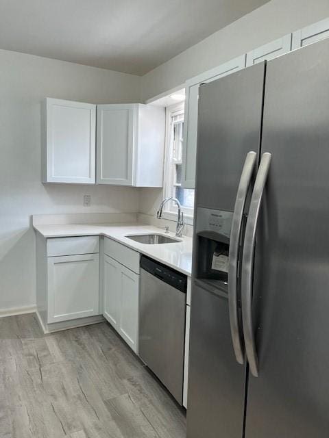 kitchen with white cabinets, a sink, light countertops, light wood-style flooring, and stainless steel appliances