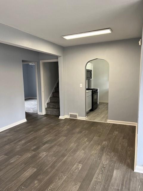 unfurnished living room with stairs, arched walkways, visible vents, and wood finished floors