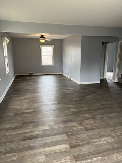 empty room with baseboards, dark wood-type flooring, ceiling fan, and visible vents