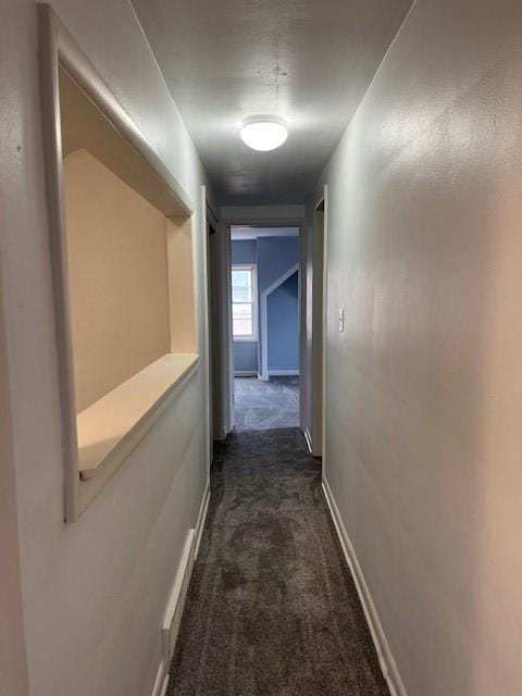 hallway with dark carpet and baseboards