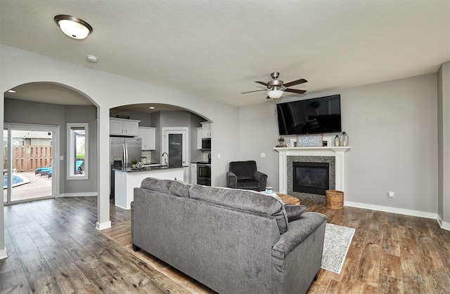 1009 NW Orchard Dr, Ankeny, IA 50023 - living room with ceiling fan, dark wood-style flooring, arched walkways, baseboards, and a glass covered fireplace