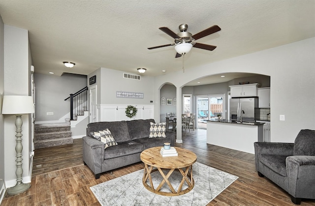 1009 NW Orchard Dr, Ankeny, IA 50023 - living room featuring ceiling fan, visible vents, arched walkways, stairway, and dark wood-style floors