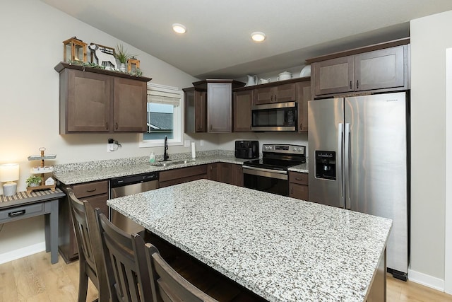 kitchen with dark brown cabinetry, a center island, light stone counters, a sink, and appliances with stainless steel finishes