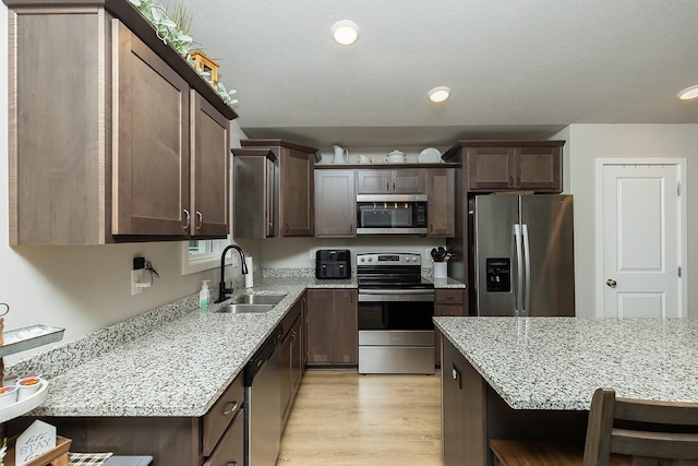 kitchen featuring dark brown cabinetry, appliances with stainless steel finishes, light stone countertops, a sink, and recessed lighting