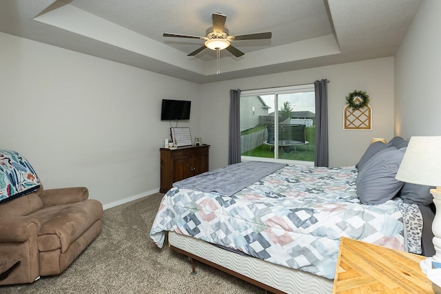 carpeted bedroom featuring baseboards, a ceiling fan, a tray ceiling, and access to outside