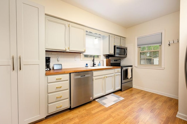 kitchen with baseboards, tasteful backsplash, a sink, wood counters, and appliances with stainless steel finishes