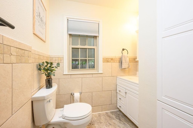 half bath with tile walls, a wainscoted wall, vanity, and toilet