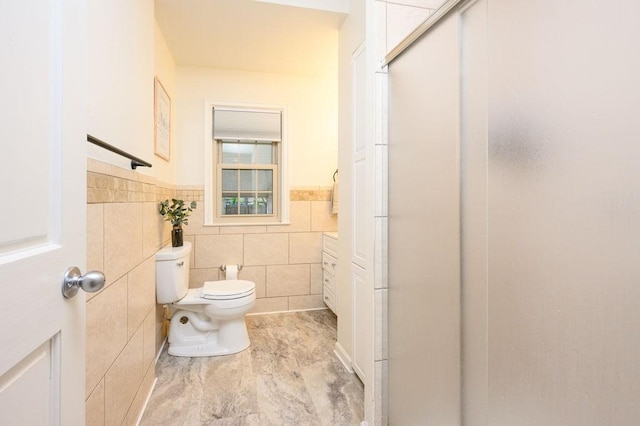 full bath with tile walls, a wainscoted wall, a shower stall, and toilet