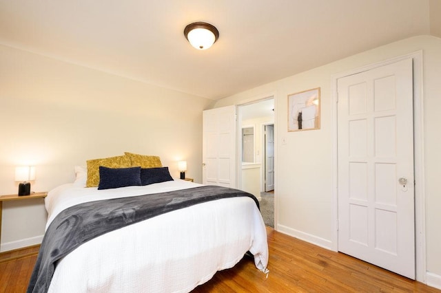 bedroom with baseboards, vaulted ceiling, and wood finished floors