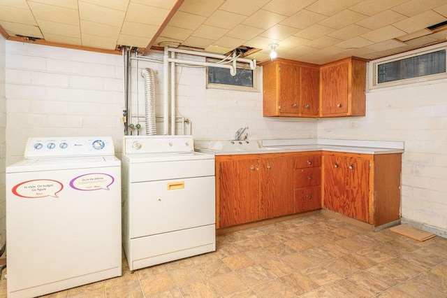 laundry room with a sink, cabinet space, concrete block wall, and washing machine and clothes dryer