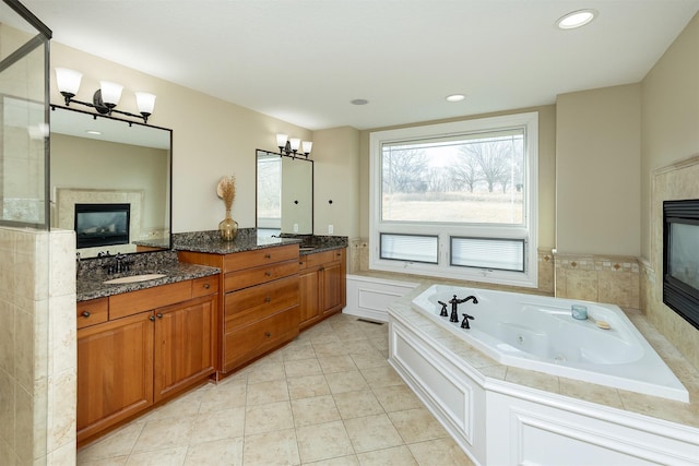 bathroom featuring double vanity, a glass covered fireplace, a sink, and a jetted tub