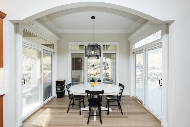 dining area with arched walkways, light wood-style flooring, and ornamental molding