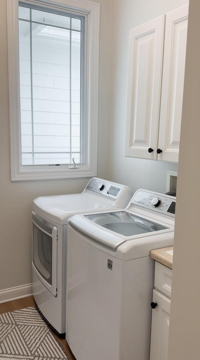 laundry room with baseboards, washing machine and dryer, cabinet space, and wood finished floors