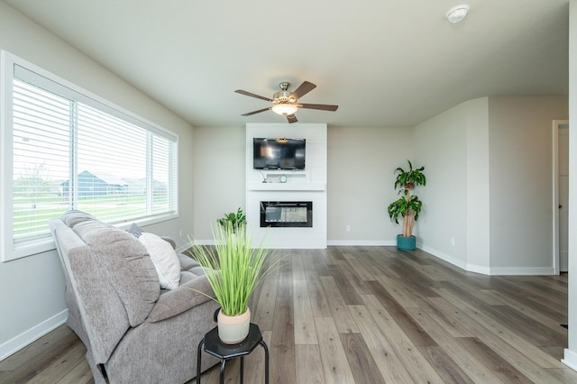 living room featuring a ceiling fan, baseboards, wood finished floors, and a fireplace