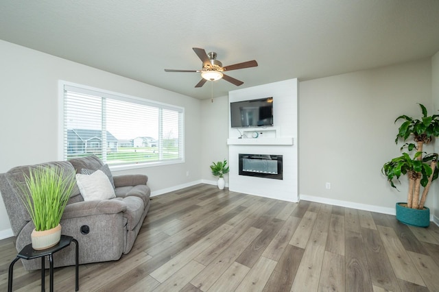 living room with baseboards, ceiling fan, wood finished floors, and a large fireplace
