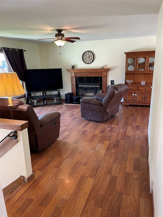 living room featuring ceiling fan, a fireplace, and dark wood finished floors