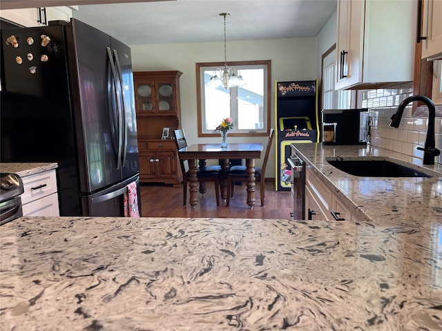 kitchen featuring light stone countertops, a sink, freestanding refrigerator, a chandelier, and dishwashing machine