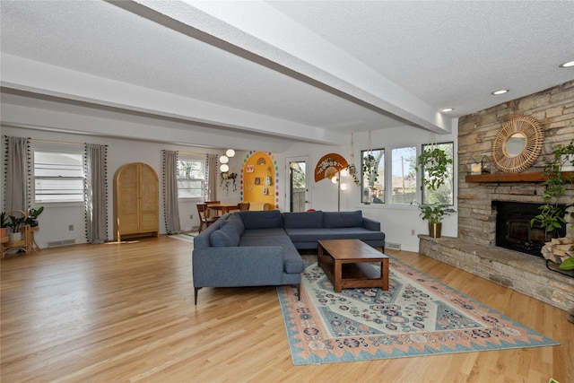 living area featuring beam ceiling, a fireplace, a textured ceiling, wood finished floors, and visible vents