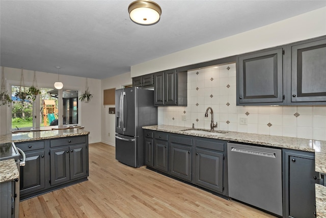 kitchen featuring backsplash, appliances with stainless steel finishes, light stone countertops, a sink, and light wood finished floors
