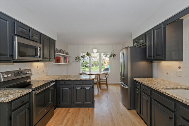 kitchen featuring backsplash, light stone countertops, a peninsula, light wood-style floors, and stainless steel appliances