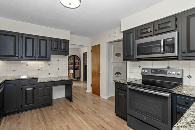 kitchen with stainless steel appliances, light stone counters, decorative backsplash, and light wood finished floors