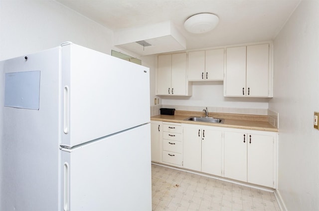 kitchen with a sink, light countertops, white cabinets, freestanding refrigerator, and light floors