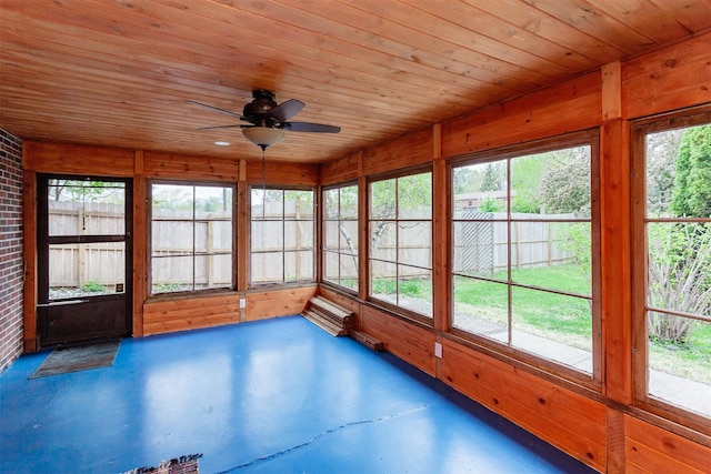 unfurnished sunroom with wood ceiling, a ceiling fan, and concrete flooring