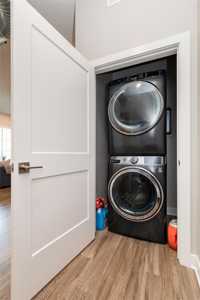 laundry room featuring wood finished floors, laundry area, baseboards, and stacked washer / drying machine