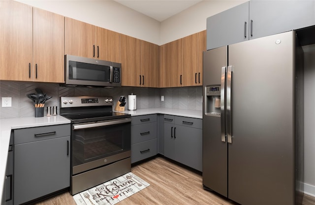 kitchen featuring light wood-type flooring, light countertops, decorative backsplash, and appliances with stainless steel finishes