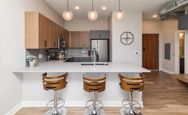 kitchen featuring a peninsula, a kitchen bar, light countertops, a sink, and appliances with stainless steel finishes