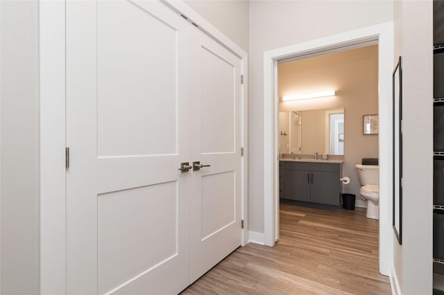 corridor with a sink, baseboards, and light wood-style flooring