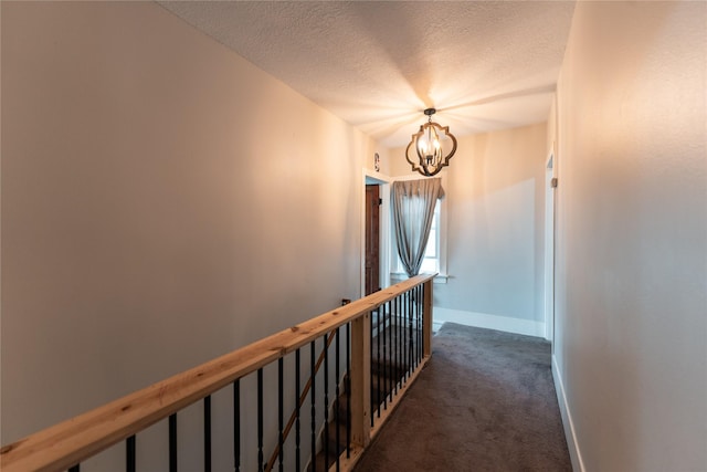 corridor with an inviting chandelier, dark carpet, baseboards, a textured ceiling, and an upstairs landing