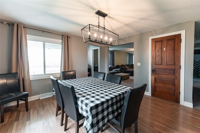 dining room featuring visible vents, baseboards, wood finished floors, and a notable chandelier