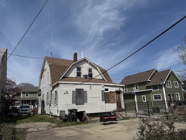 back of house featuring a gambrel roof, a chimney, and fence