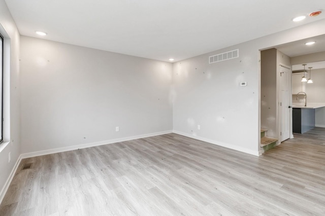 empty room featuring a sink, light wood-style flooring, recessed lighting, baseboards, and visible vents