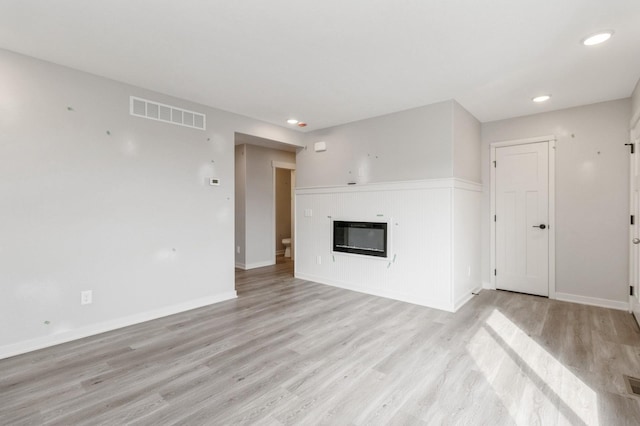 unfurnished living room with visible vents, a glass covered fireplace, baseboards, recessed lighting, and light wood-style flooring