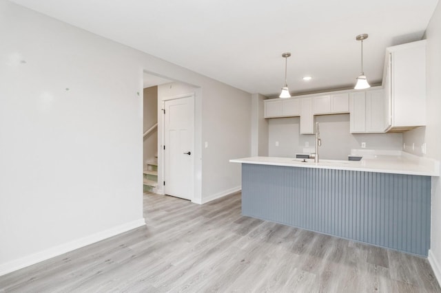 kitchen featuring light countertops, a peninsula, baseboards, white cabinetry, and light wood-type flooring