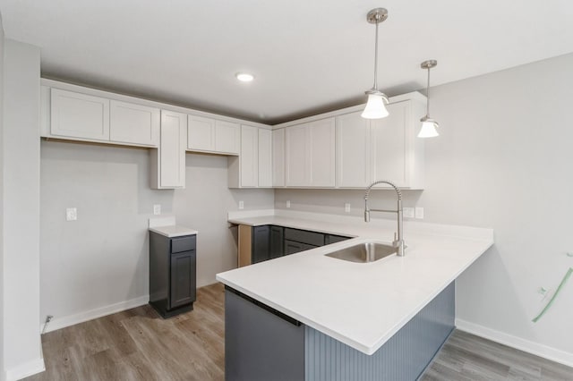 kitchen with a sink, baseboards, white cabinets, a peninsula, and light wood-style floors