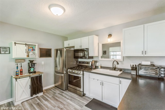 kitchen featuring appliances with stainless steel finishes, a sink, white cabinets, light wood finished floors, and a textured ceiling