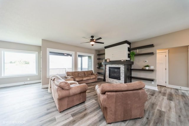 living room featuring baseboards, ceiling fan, light wood-type flooring, and a stone fireplace