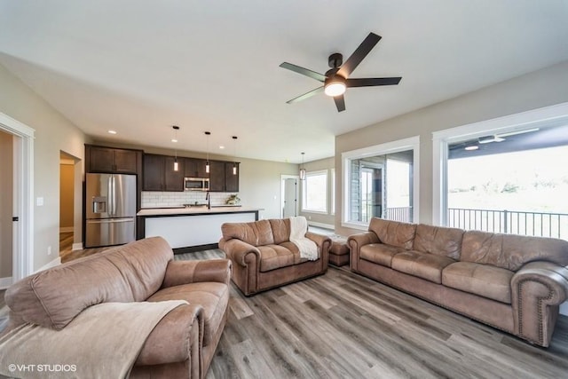 living area with baseboards, ceiling fan, and light wood-type flooring